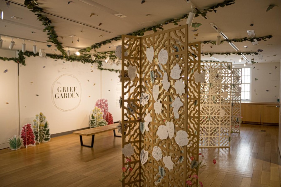 Mandala-style wooden blinds decorated with floral designs and short notes in the foreground and a poster saying “Grief Garden” in the background.