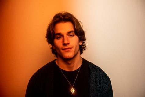 A headshot of Jonah Kagen. He is wearing a black sweater and looking directly at the camera. The picture has an orange gradient filter.