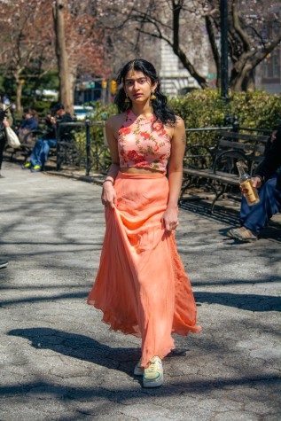 A full body portrait of Aarna Dixit wearing a peach-colored lehenga, traditional Indian gold jewelry and yellow sneakers. She is standing in front of park benches.