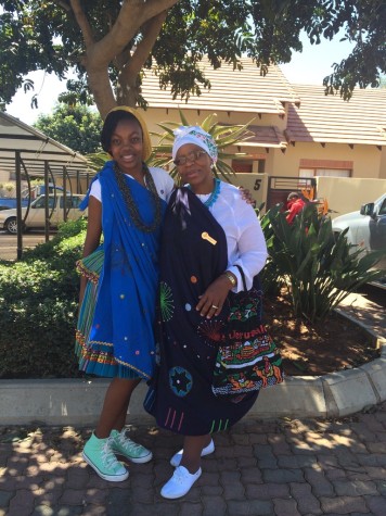 Mika Chipana (left) and her grandmother (right) dressed in traditional attire standing in the shade of a tree.