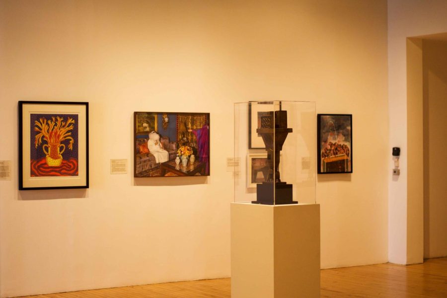 Five art pieces displayed in frames on a white wall inside the Grey Art Gallery. In the foreground, a clear encased sculpture in the center of the room.