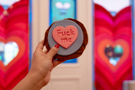 A chocolate chip cookie with blue fondant and a pink heart as decoration. In the heart are the words “Fuck Me.”