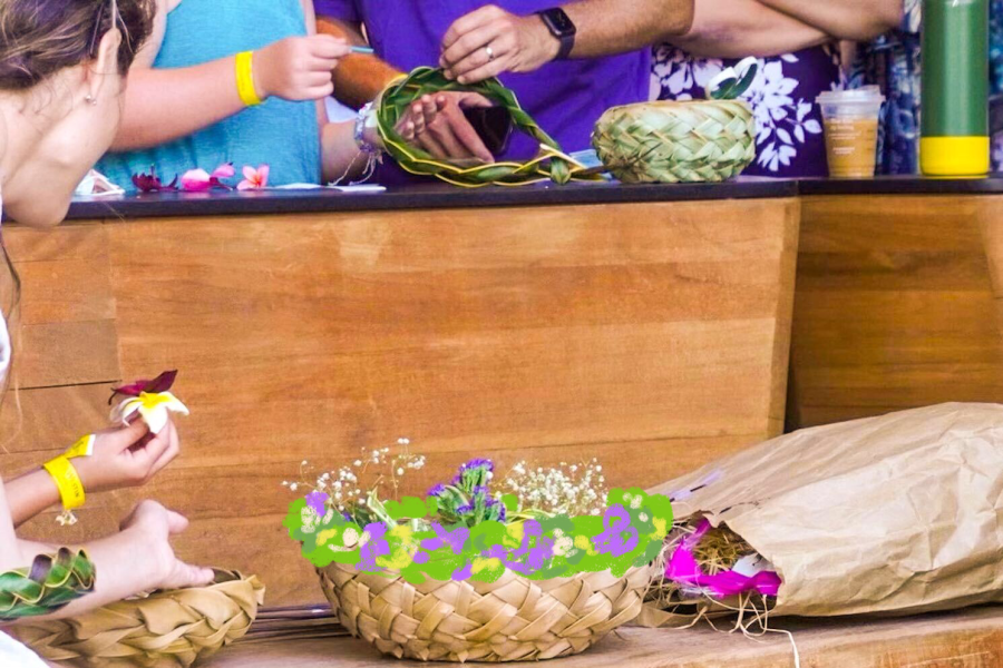 A basket of purple flowers in the foreground and peoples hands holding flower petals in the background.