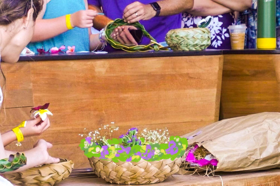 A basket of purple flowers in the foreground and people's hands holding flower petals in the background.