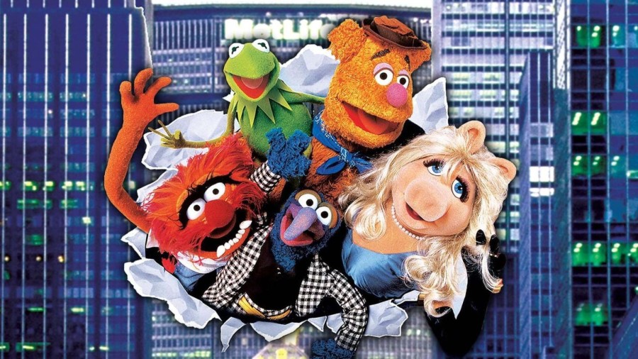 A group of five excited Muppets rip through a paper background with an image of New York City skyscrapers.