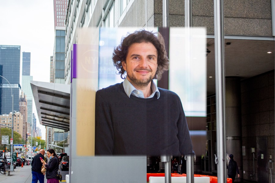 A portrait of David Sabatini wearing a blue sweater and button down overlaid in front of the NYU Langone Health building. People are walking in the background outside the building and a large sign with “NYU Langone Health is in the front.