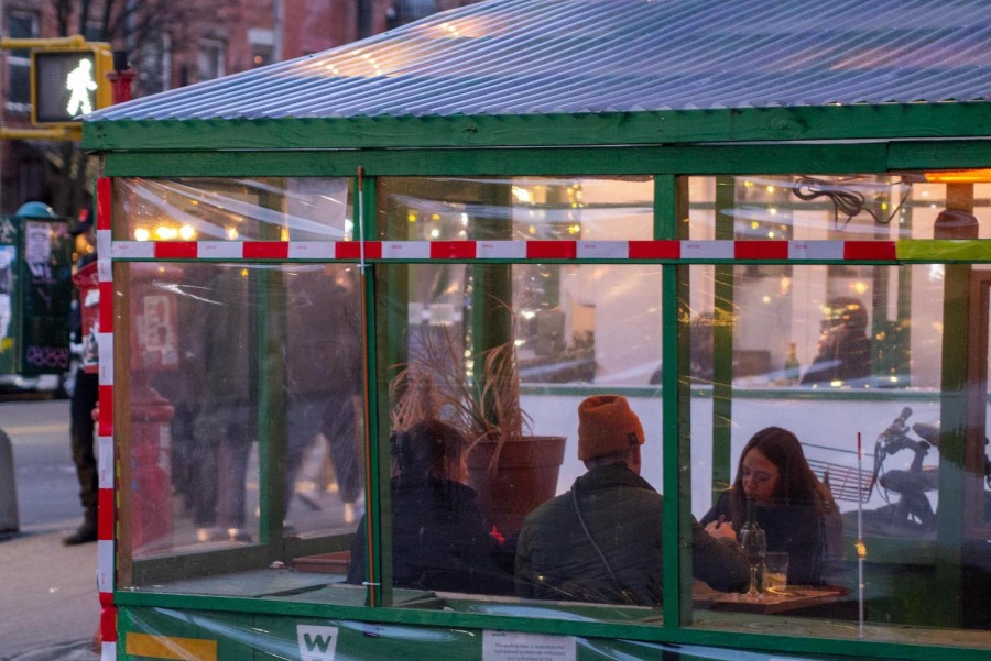 A green outdoor dining structure on the street. Inside, three people are eating at a table.