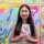 Portrait of Grace Xiang holding up an assortment of stickers. Xiang is standing in front of an abstract multicolored background.