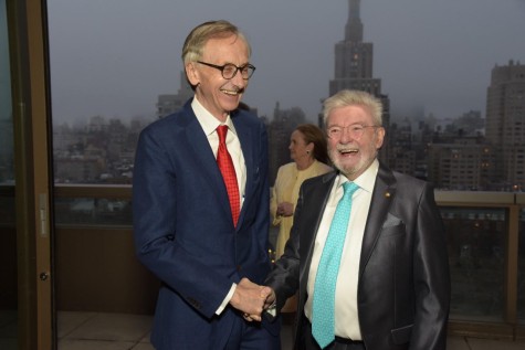 To the left, Ted Smyth wears a blue suit, a red tie and black glasses. Smyth is shaking hands and looking towards the right at James Galway, who is wearing a black suit and a blue tie.