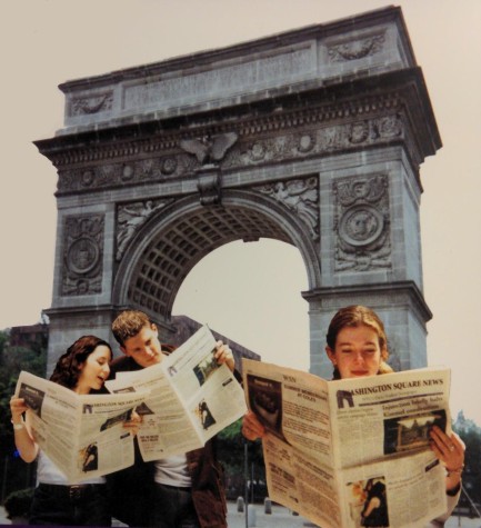 A photograph of three people holding up print copies of the Washington Square News. The Washington Square Arch is visible in the background.