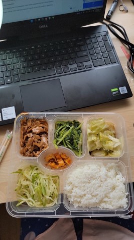 An overhead view of a desk with a boxed meal with food separated into different sections.