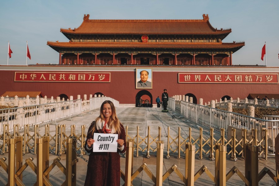 Lexie Alford, the youngest person ever to visit every country, holds up a sign that reads "Country #111" in front of the The Forbidden City palace complex in Beijing, China.