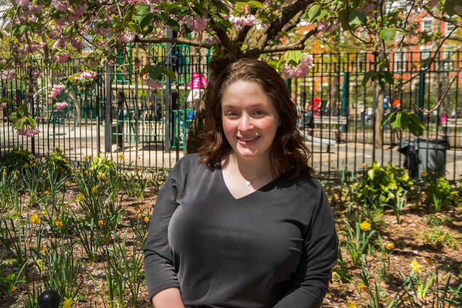 A portrait of Laura Derbonne standing in front of a cherry blossom tree at Washington Square Park.