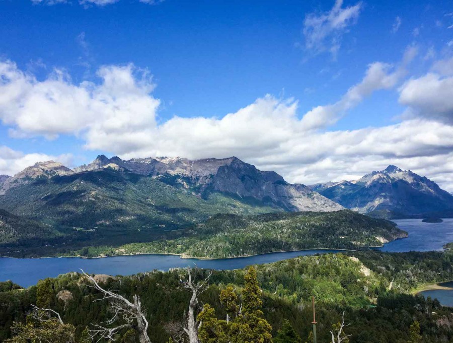 A view of the green and brown mountains and the surrounding blue lake in Bariloche, Argentina.