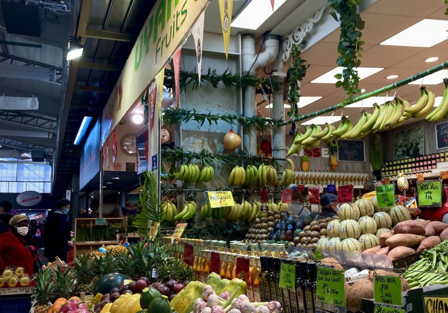 Blue crates filled with various fruits and vegetables sit in front of a French grocery store.