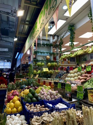 Blue crates filled with various fruits and vegetables sit in front of a French grocery store.