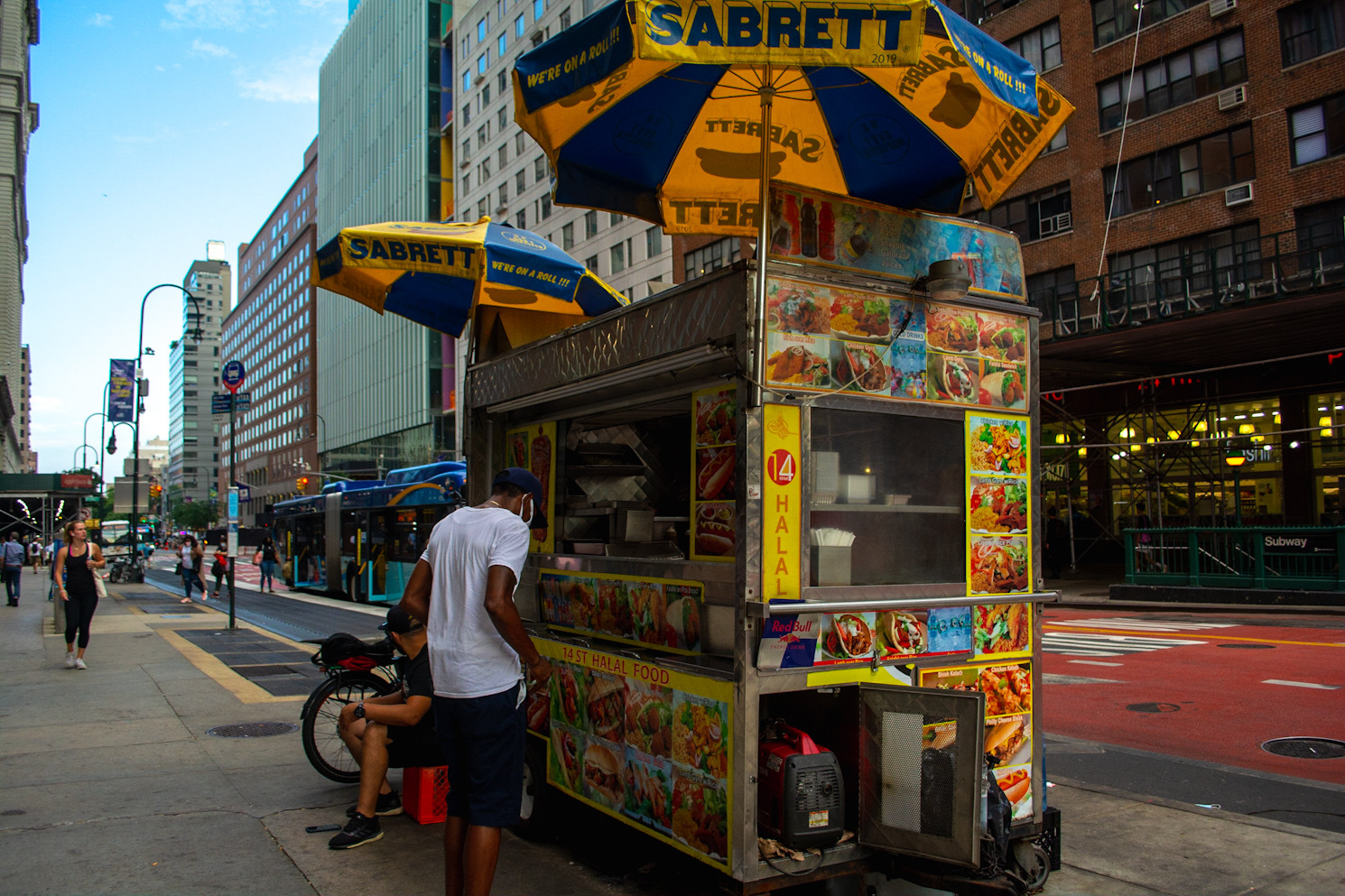 A halal food cart in the foreground, and East 14th Street in the background.