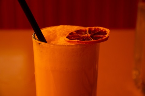 A mocktail glass with a dried citrus fruit on top against a yellowish background.