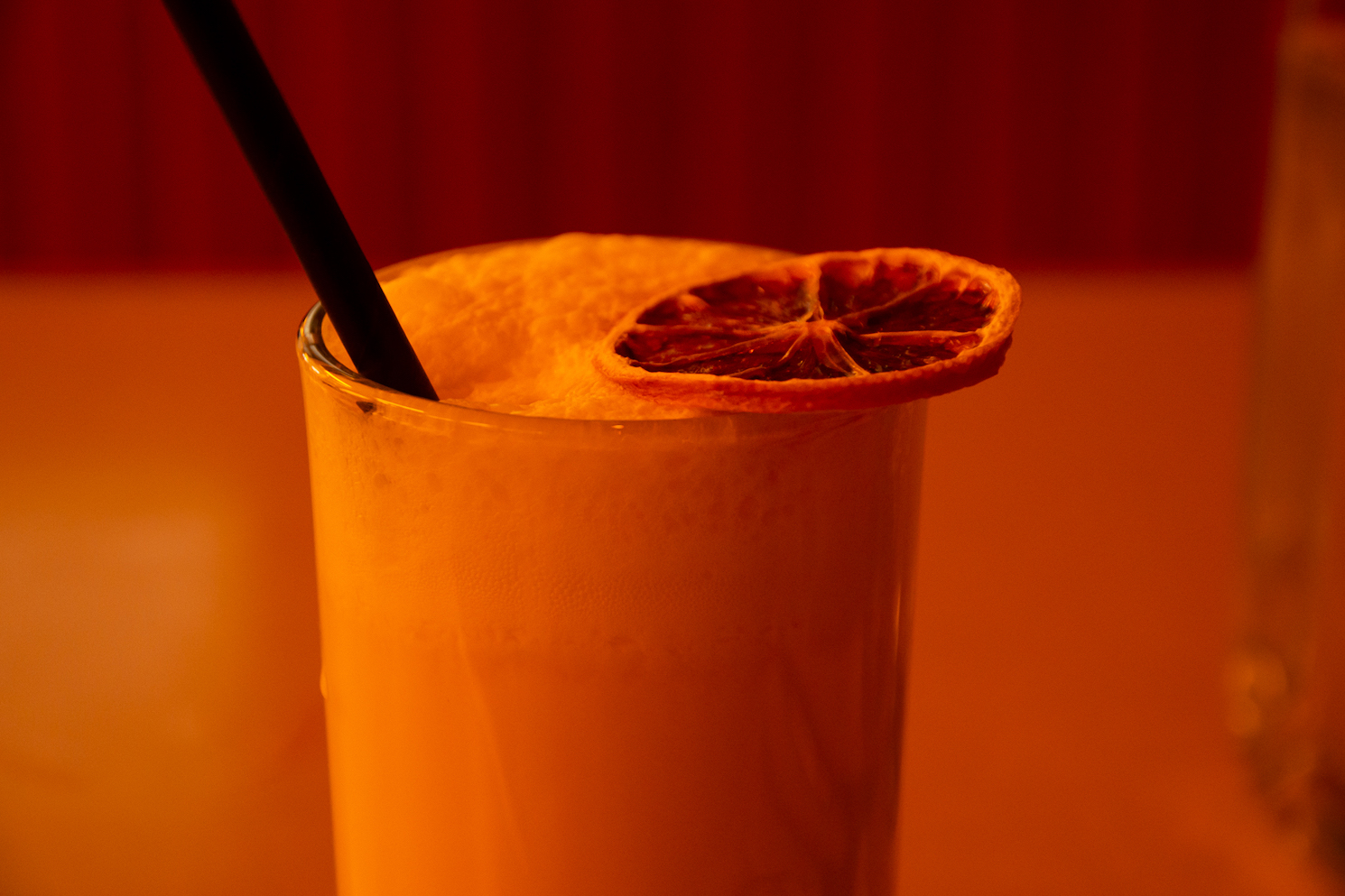 A mocktail glass with a dried citrus fruit on top against a yellowish background.