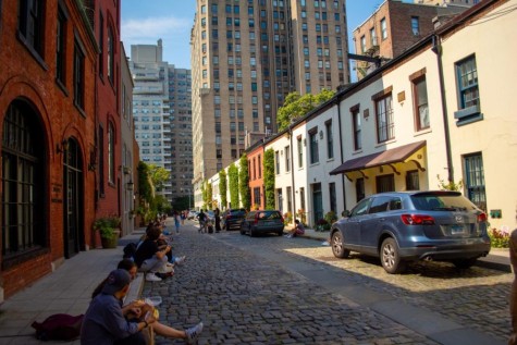 A vertical view of Washington Mews and people sitting on the sidewalk and talking.