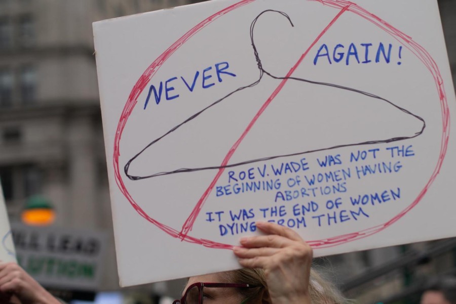 A sign with a crossed out hanger. The sign reads “Never Again! Roe v. Wade was not the beginning of women having abortions. It was the end of women dying from them.”