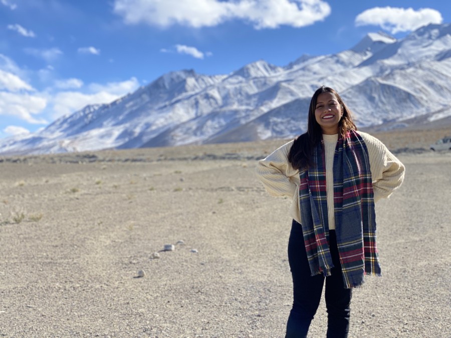 Astha Rajvanshi wearing a plaid scarf standing in front of mountains in India.