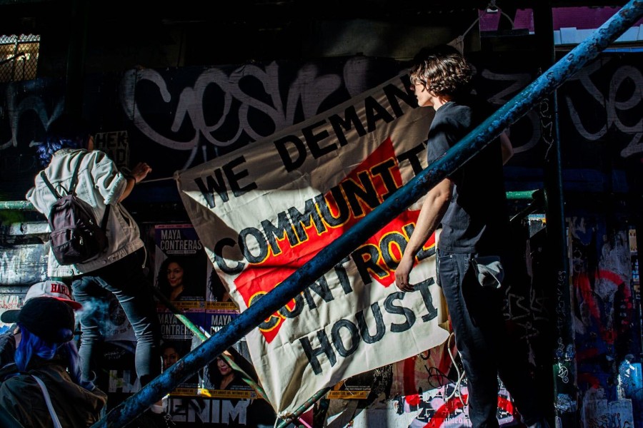 Two people hang up a protest banner on the exterior façade of a building covered with scaffolding.