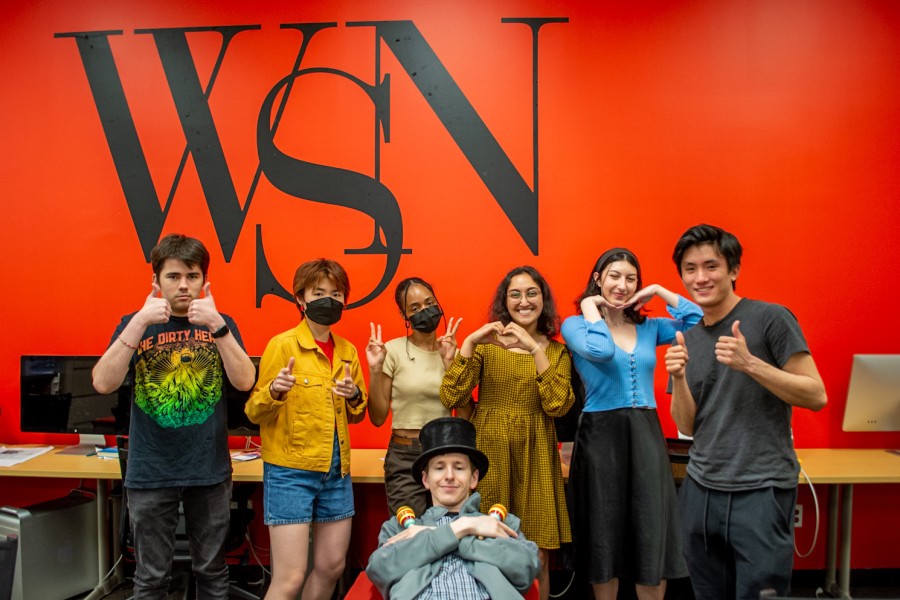 A group photo of (Left to right, top to bottom) Jake Capriotti, Caitlin Hsu, Charitssa Stone, Sabrina Choudhary, Isabella Armus, Sho Matsuyama and Max Tiefer in front of the WSN logo in the WSN office.