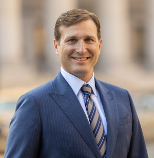 Dan Goldman, standing in a blue suit and tie for a headshot.