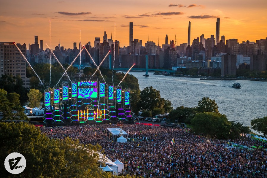 Fireworks launching into the sky in front of a stage and a large crowd, with the Manhattan skyline in the background.