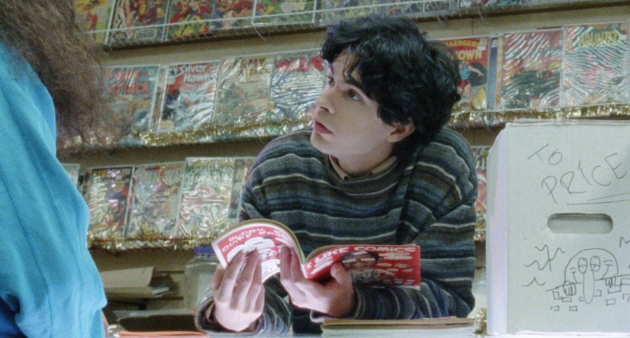 Person holding a red-covered comic book is looking up, standing in front of a shelf of cartoon books.
