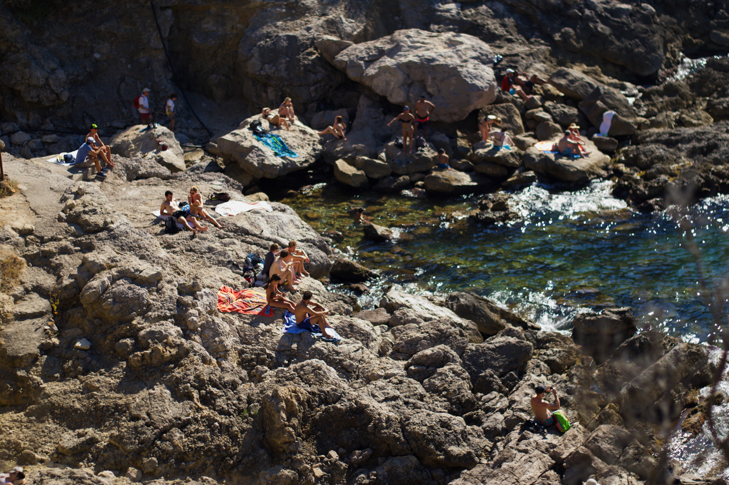People sitting on a rocky coast facing shallow water.