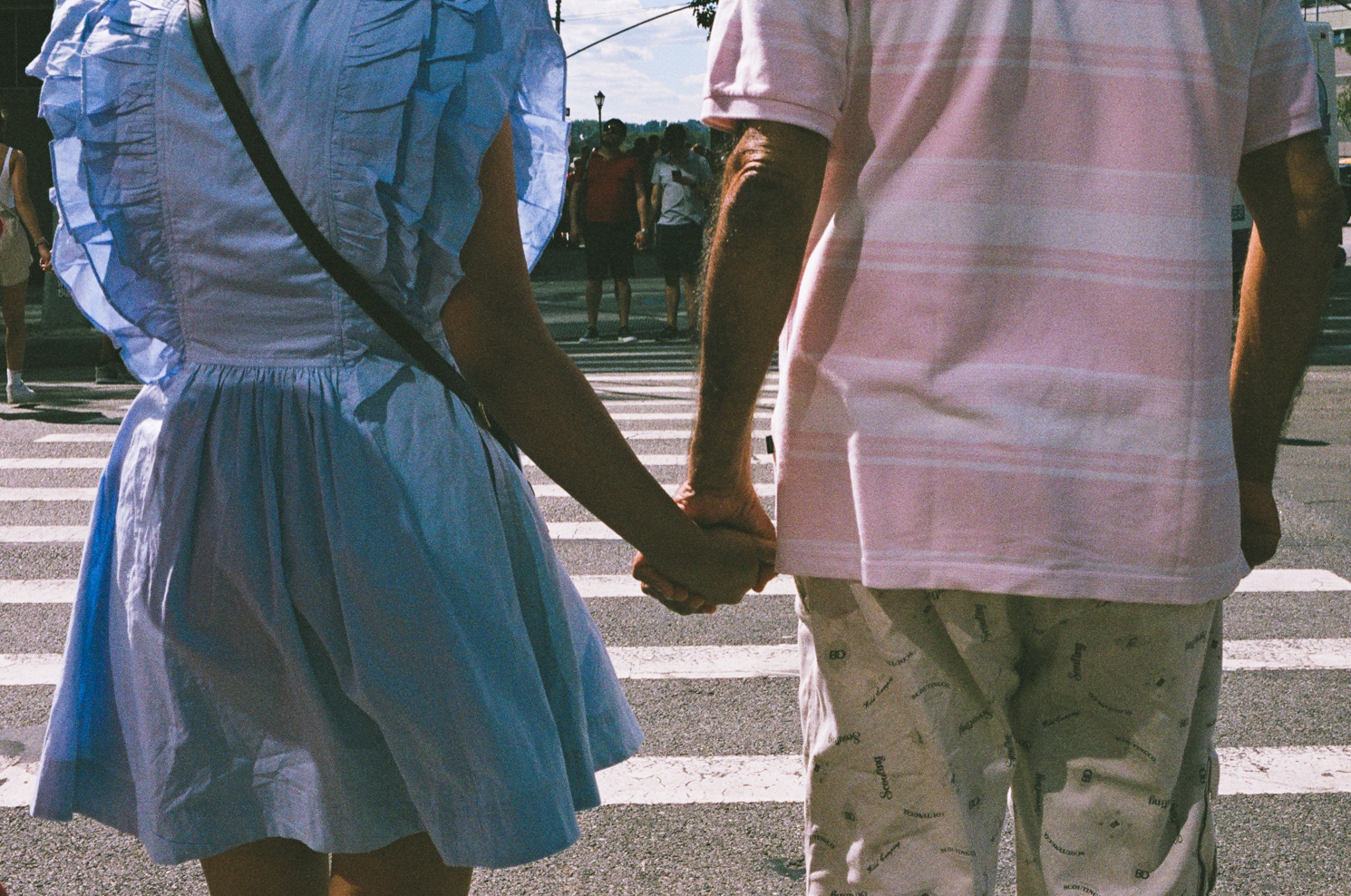 A woman in a light blue dress and a man in a pink, striped shirt holding hands at an intersection.