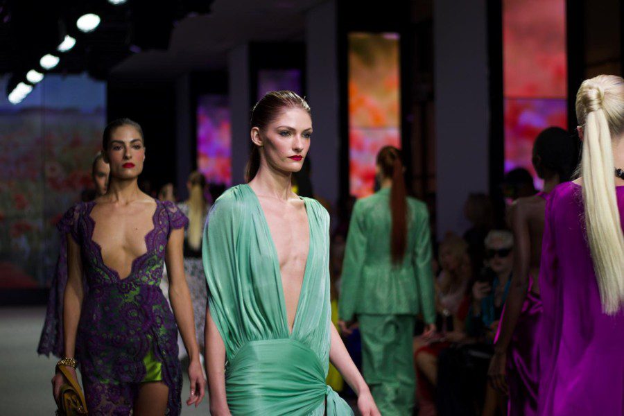 A model walks down the runway in a long green dress with a low neckline.