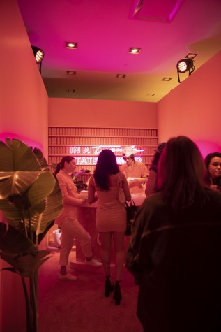 A neon pink and orange lit room with a man behind the counter serving coffee.