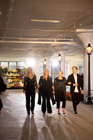 Four people walk down the runway holding hands, they are all dressed in black.