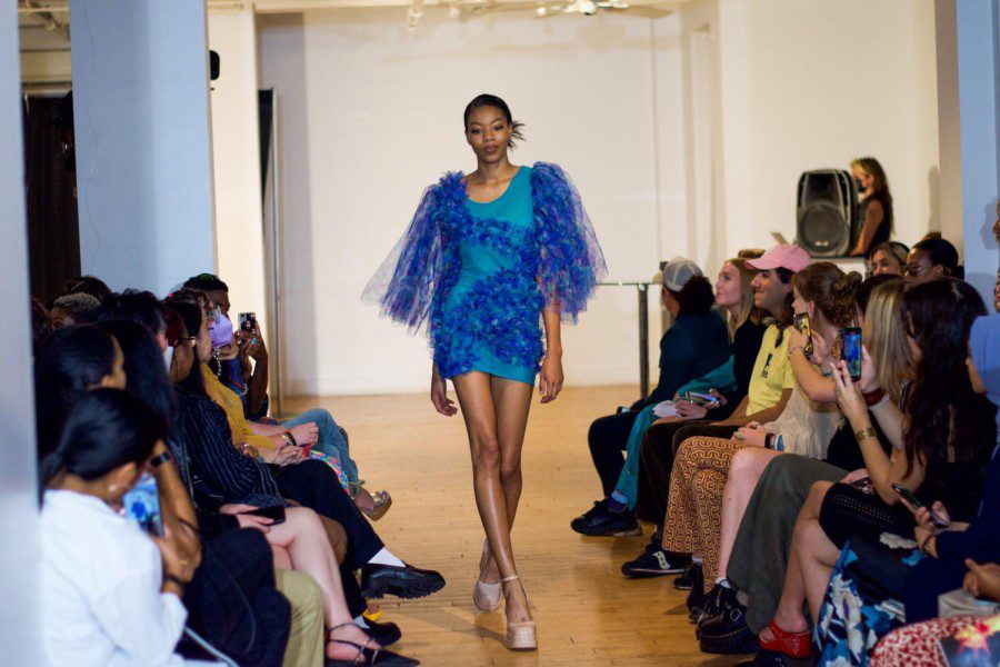 A model walks down the runway in a blue dress with purple tulle sleeves.