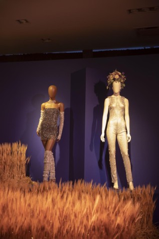A mannequin wearing a mini silver dress, and another one next to it wearing a silver jumpsuit and purple, white, pink, and green flower crown.