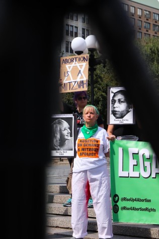 A woman wearing a shirt that reads “abortion on demand and without apology” holds a sign.