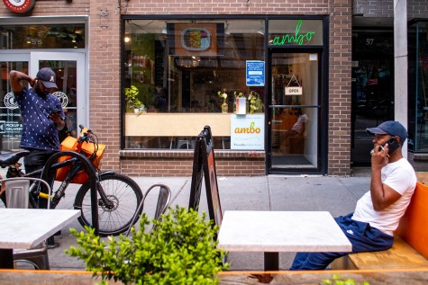 A man with a blue baseball cap taking a call while sitting at a table in front of ambo.