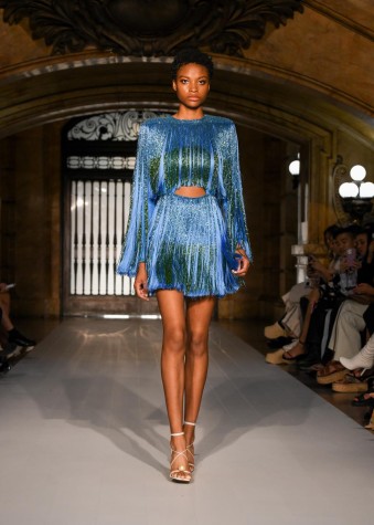A woman walks the runway in a blue hand-beaded ombre fringe mini dress