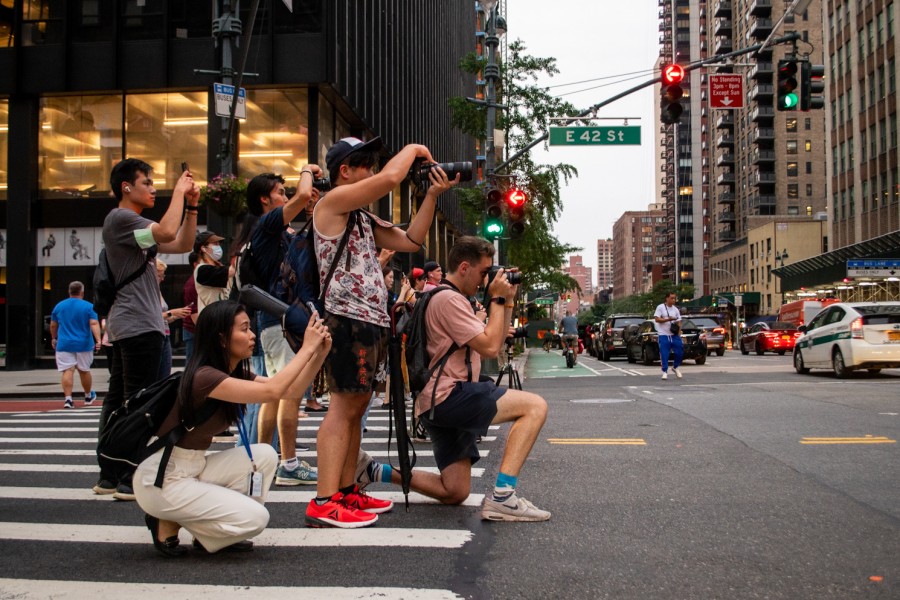 A group of photographers standing and crouching on the zebra-striped crosswalk.