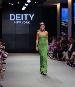 Woman walks down the runway in a green dress.