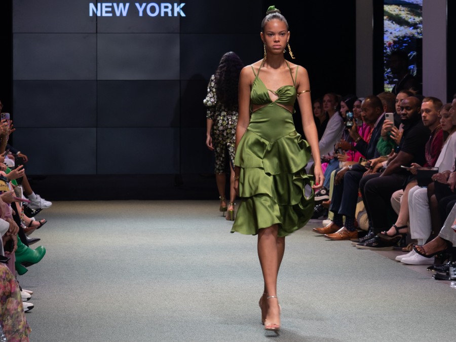 Woman walks down the runway in a ruffled olive dress.