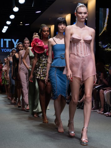 Women modeling the Deity New York Spring/Summer 2023 collection walk down the runway in single file. A woman in a blush ensemble and silver heels is seen in the front.