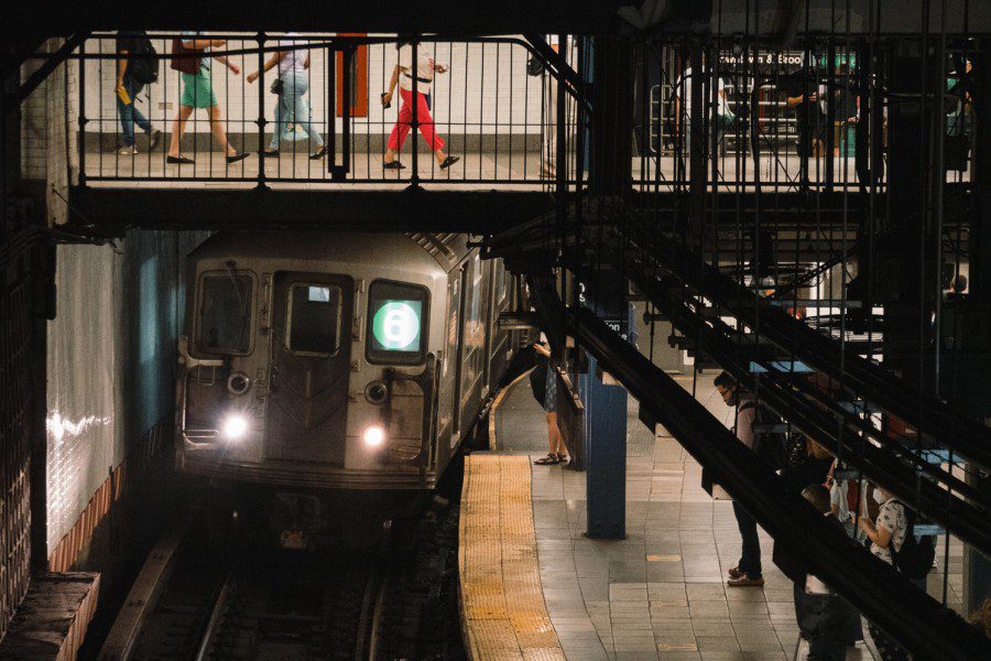 The 6 subway train arrives at the Union Square station. People stand on the platform and walk on the overpass.