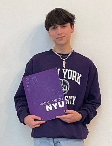 Giancarlo Arias stands holding an NYU welcome packet and wearing an NYU purple hoodie.