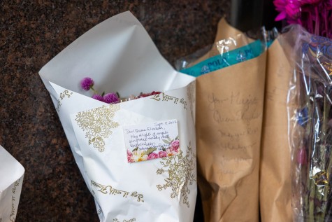 A sticky note to the Queen is pasted on a bouquet of flowers amid a memorial.