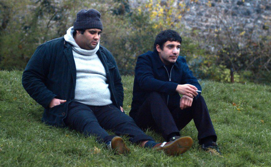 Aurélien Gabrielli, who plays Labidi El Morchedi, and Léon Cunha Da Costa, who plays Aleksei Kouyenski, sit on a grassy hill dressed in winter outfits smoking a cigarette in a still from “The World After Us.”