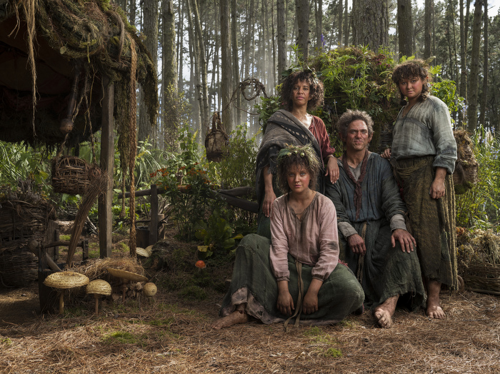 Markella Kavenagh who plays Elanor ‘Nori’ Brandyfoot, Sara Zwangobani who plays Marigold Brandyfoot, Dylan Smith who plays Largo Brandyfoot and Megan Richards who plays Poppy Proudfellow pose in front of a forest background.